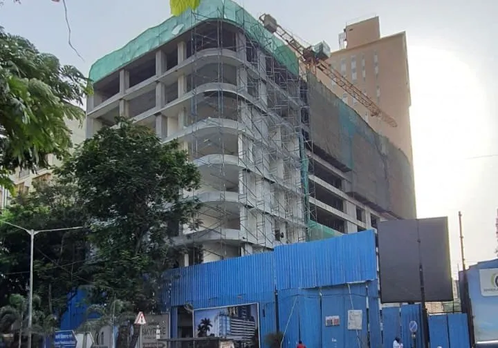 Photograph of the podium under construction behind blue hoarding, a tower crane above